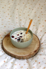 Breakfast bowl with oatmeal, berries, chia seeds and coconut chips on a bed with floral sheets. Selective focus.