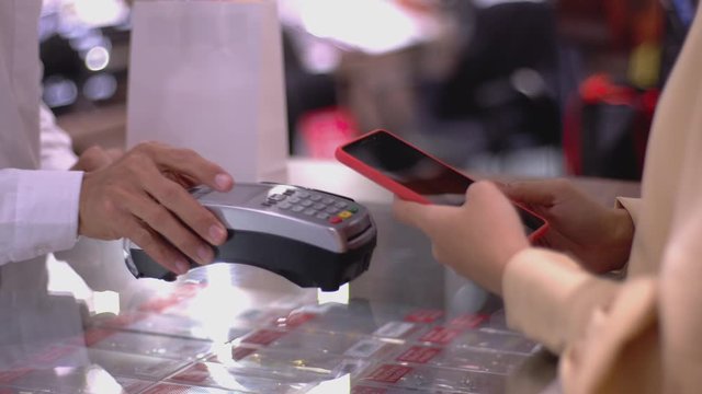 An upwardly mobile Asian Muslim woman using a mobile phone to pay for a product at a sale terminal with nfc identification payment for verification and authentication