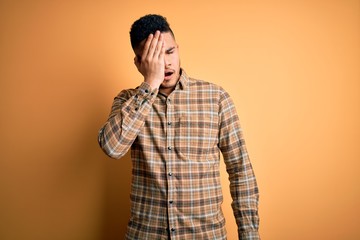 Young handsome man wearing casual shirt standing over isolated yellow background Yawning tired covering half face, eye and mouth with hand. Face hurts in pain.