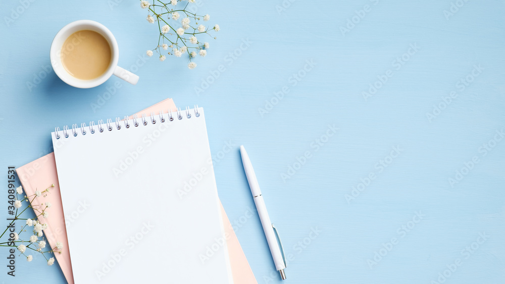 Wall mural flat lay, top view feminine workspace with blank notepad, cup of coffee, pen and flowers on blue bac