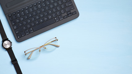 Fototapeta premium Stylish feminine workspace with laptop computer keyboard, watches, glasses on blue background. Modern home office desk, freelancer workplace. Flat lay, top view, copy space