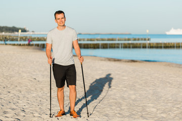 Pretty young man resting after nordic walking on the beach. Healthy sport life concept