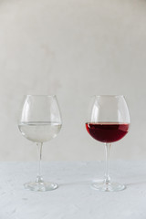 two wine glasses on a grey background one with red wine and the other with water