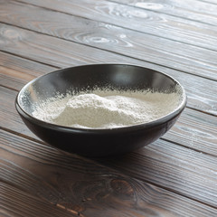Flour in black bowl. Dark wood background.