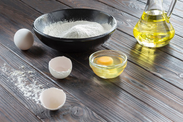 Black bowl with flour. Glass bottle with butter, eggs, eggshell,