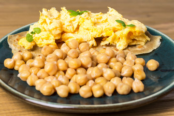 Chickpeas and  scrambled eggs on pita bread. Green plate.  Close up.