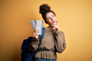 Beautiful tourist woman with curly hair and piercing wearing backpack holding boarding pass serious face thinking about question, very confused idea