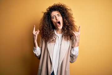 Young beautiful brunette woman with curly hair and piercing wearing casual t-shirt and diadem shouting with crazy expression doing rock symbol with hands up. Music star. Heavy concept.