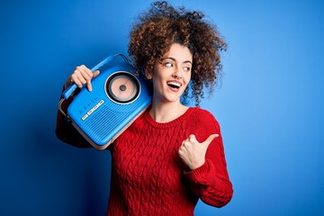 Obraz premium Young beautiful woman with curly hair and piercing listening to music using vintage radio pointing and showing with thumb up to the side with happy face smiling
