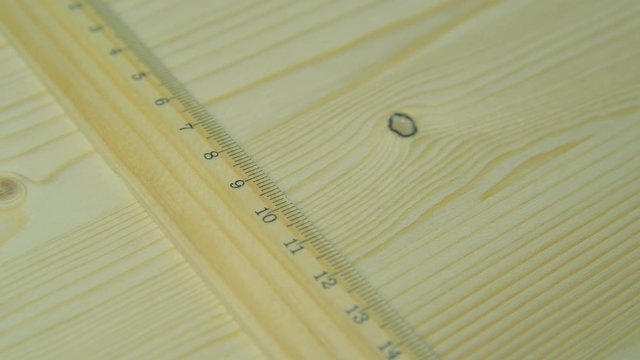 A man makes a mark on the board with a pencil and a ruler.