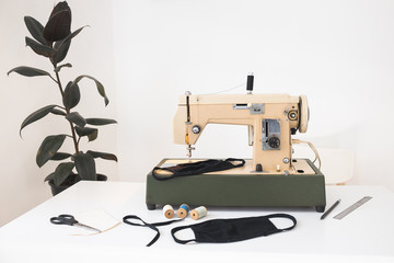 Beige sewing machine the process of sewing a protective medical mask at home workplace with a house plant ficus