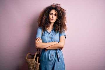 Young beautiful woman with curly hair and piercing wearing denim dress and wicker bag skeptic and...