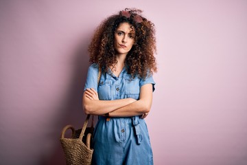 Young beautiful woman with curly hair and piercing wearing denim dress and wicker bag skeptic and nervous, disapproving expression on face with crossed arms. Negative person.