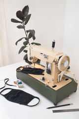 Beige sewing machine the process of sewing a protective medical mask at home workplace with a house plant ficus