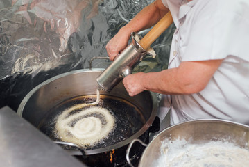 Woman works in a cafeteria frying dough in hot oil. Hot churros