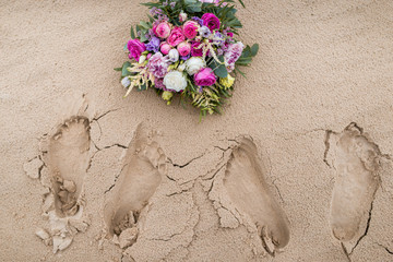 footprints in the sand with a wedding bouquet