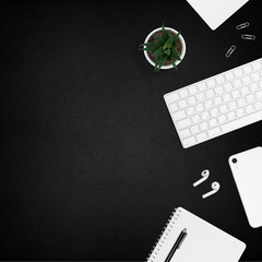 Flat layout of workplace. White office supplies and a plant on black leather background