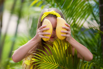 Lovely girl in yellow swimsuit holds a yellow mango on vacation in the tropics