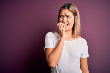 Young beautiful blonde woman wearing casual white t-shirt over purple isolated background looking stressed and nervous with hands on mouth biting nails. Anxiety problem.