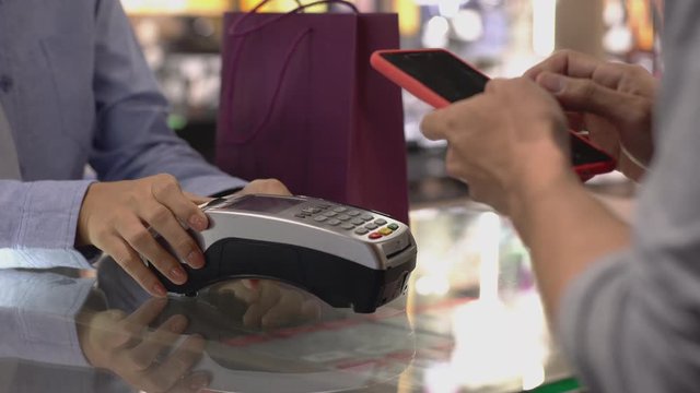 An upwardly mobile Asian Muslim man using a mobile phone to pay for a product at a sale terminal with nfc identification payment for verification and authentication
