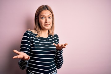 Young beautiful blonde woman wearing casual striped sweater over pink isolated background clueless...