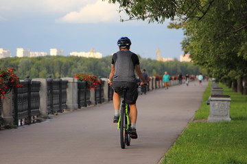 One cyclist man in sportsewar with helmet rides on a bicycle on asphalted alley Nagatinskaya embankment of the Moscow River on a summer day, back view. Urban active recreation of Muscovites