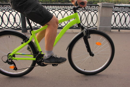 One cyclist man in rides on a bright yellow hardtail mountain bike close up on asphalted road quayside on a summer day, waist-high side view, icycle ecological transport