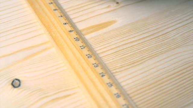 A carpenter makes marks on a wooden wall to install a metal coat hook.