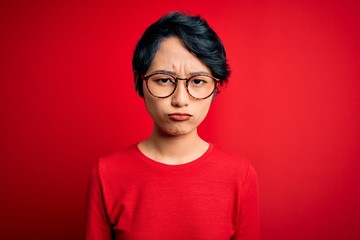 Young beautiful asian girl wearing casual t-shirt and glasses over isolated red background depressed and worry for distress, crying angry and afraid. Sad expression.