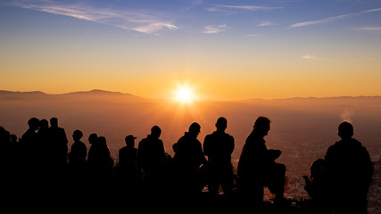 Group of people backlit during a sunset with the sun and mountains in the background. Viewpoint of San Miguel Alto, Granada.