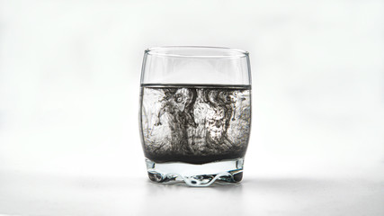 Black ink dropping into a glass of water on a white background.