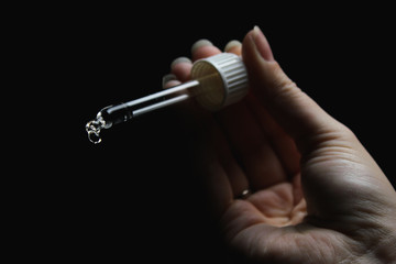 female with beautiful nails hold pipette isolated on black background