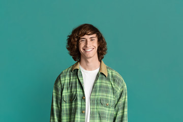 Attractive young guy with curly hair smiling on color background