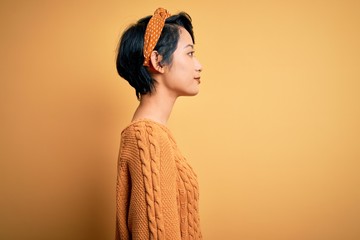 Young beautiful asian girl wearing casual sweater and diadem standing over yellow background...
