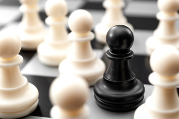 Leadership, diversity and individuality concept with black pawn surrounded by many white pawns on crowded chess board