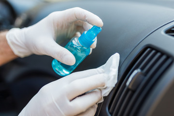 Man cleansing car dashboard vent grille air duct and spraying with disinfection liquid.