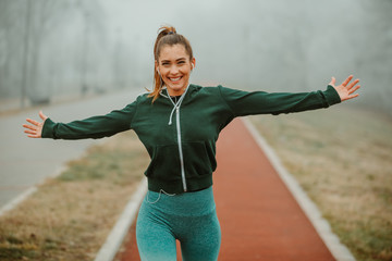 Fototapeta na wymiar Close photo of young excited woman runner with beautiful smile and outstretching arms after outdoor run on foggy morning.