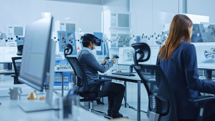 Modern Factory: Industrial Design Engineer Wearing Virtual Reality Headset and Holding Controllers, Uses VR technology for Industrial Design, Development and Prototyping in CAD Software on Computer.