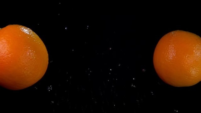 Two juicy oranges are flying and colliding with each other rising splashes of water on the black background in slow motion