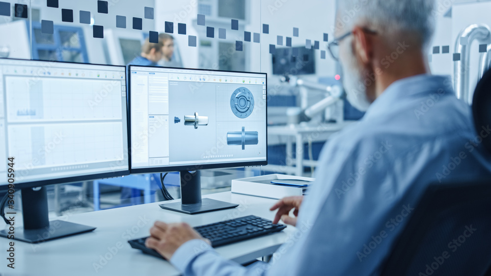 Fototapete Over the Shoulder: Senior Heavy Industry Engineer Working on Personal Computer, Screen Shows CAD Software with 3D Prototype of Electric Engine. Industrial Factory with High-Tech CNC Machinery