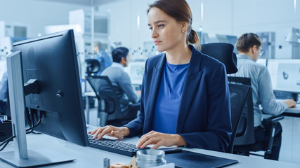 Modern Factory Office: Portrait of Young and Confident Female Industrial Engineer Working on Computer. Industrial Factory with Industry Design Engineers Working on Computers, CNC Machinery Workshop