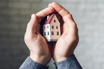 Male hands holding and protecting small toy house. Conceptual image of insurance and staying home safe during Corona virus quarantine lockdown