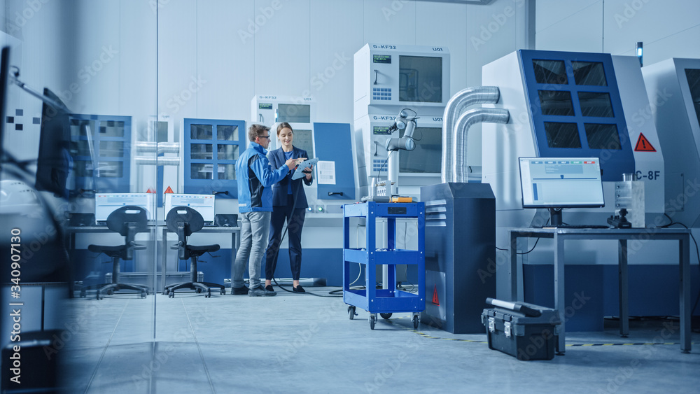 Poster Modern Factory: Female Project Manager and Male Engineer Standing, Talking and Using Tablet Computer for Programming Robot Arm Assembly Line. Contemporary Facility with High Tech CNC Machinery