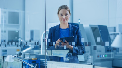 Modern Factory Office: Portrait of Young and Confident Female Industrial Engineer Standing and Holding Digital Tablet, She Smiles Charmingly at Camera. Industrial Factory with CNC Machinery Workshop