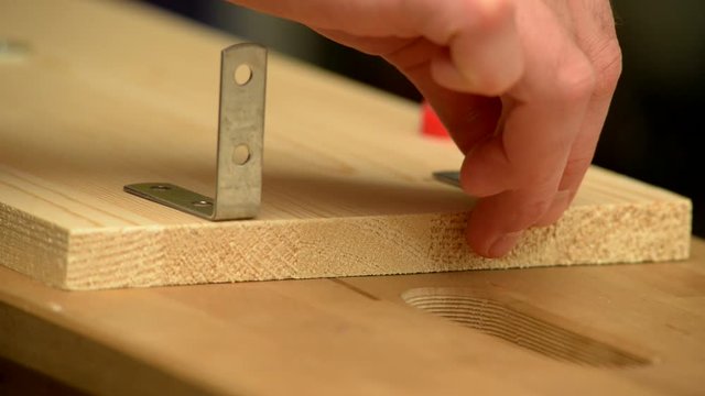 Close-up. A man uses an electric screwdriver to tighten the screws in a wooden board.