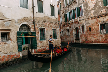 Fototapeta na wymiar The gondolier controls a beautiful gondola sailing through a narrow channel where the water is green | VENICE, ITALY - 16 SEPTEMBER 2018. 