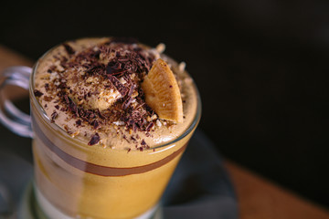 Detail of the upper part of a Dalgona coffee, presented with a cookie and pieces of noir chocolate. Close-up