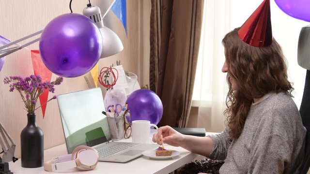 Woman celebrating her birthday through video call virtual party. Lits and blows out candle. Authentic decorated home workplace. Handheld shot with gimbal. Coronavirus outbreak 2020.