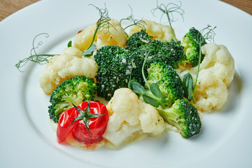 Diet and veggie snack - steamed vegetables (broccoli, cauliflower and cherry tomatoes) in a white plate on a wooden background