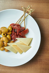 Appetizing Italian antipasto - sun-dried tomatoes, olives and parmesan in a white plate on a wooden background